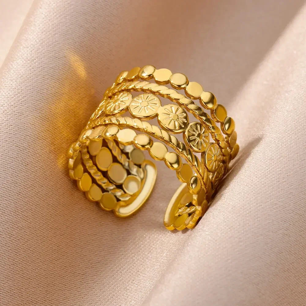 Nahaufnahme eines mehrlagigen geometrischen offenen Rings in Gold auf weichem beigem Stoff.