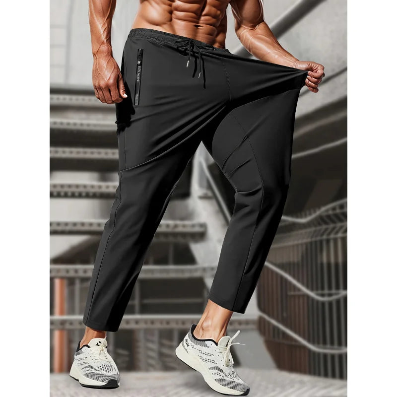 A muscular man wearing black high-stretch joggers with zippered pockets, standing in a gym setting.
