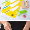 A yellow cutting board holds a white plastic fruit knife set with various colored blades next to fresh produce.