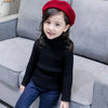 A young girl wearing a black knit turtleneck sweater and blue jeans, with a red beret, sitting on a gray sofa.