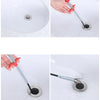A hand uses a flexible drain snake tool to clear a clog in a white ceramic sink.