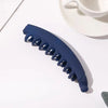 Clip de plátano acrílico esmerilado azul oscuro para el cabello sobre superficie blanca, junto a una taza y platillo blancos.