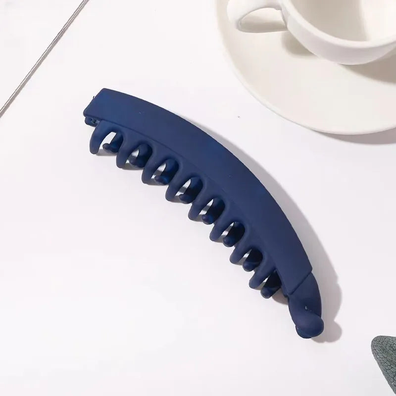 Clip de plátano acrílico esmerilado azul oscuro para el cabello sobre superficie blanca, junto a una taza y platillo blancos.