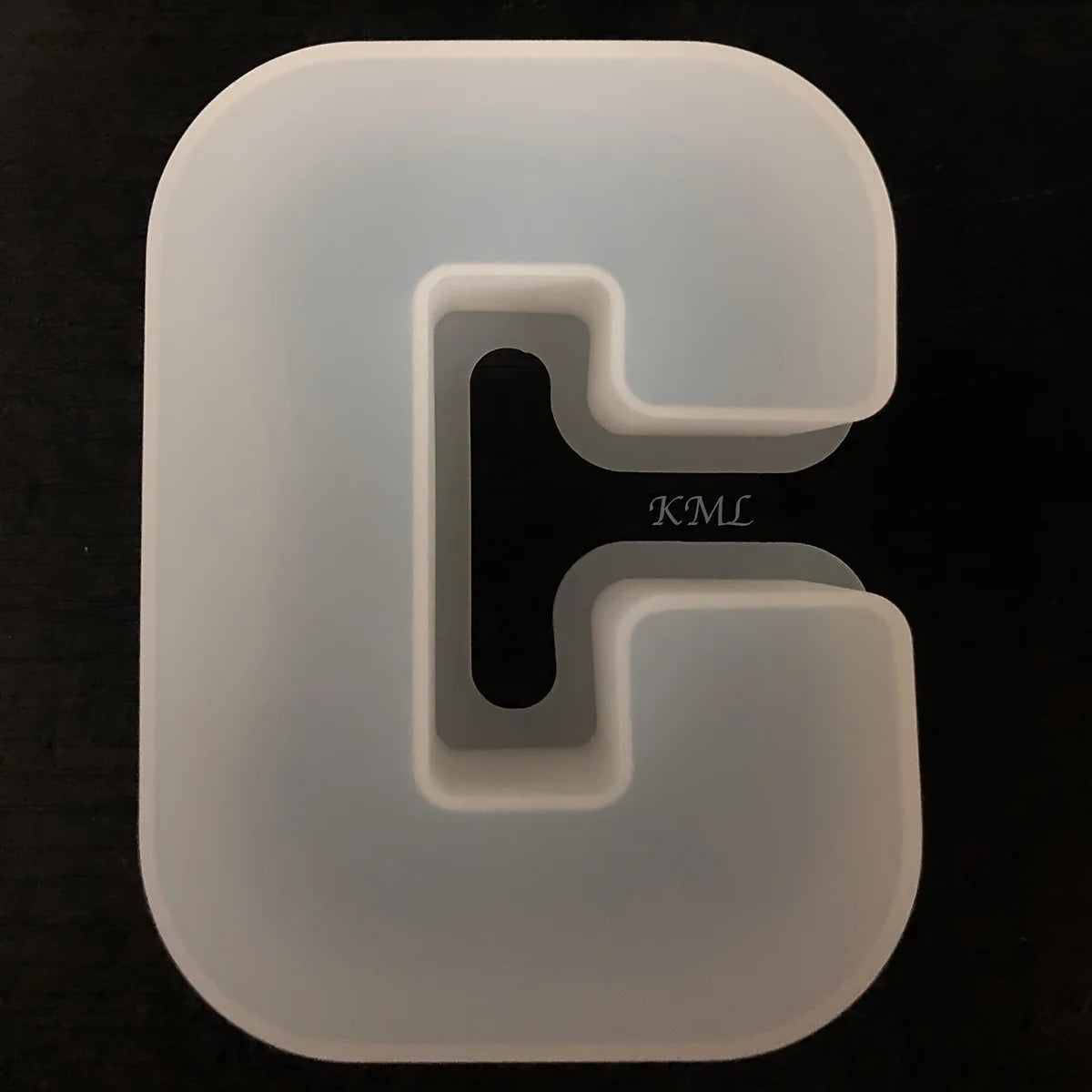 Klares Silikonform mit eingeprägtem Buchstaben G und Text KML auf dunklem Hintergrund.