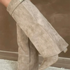 A close-up of beige knee-high boots with a chunky heel and a metal buckle worn on a leg.