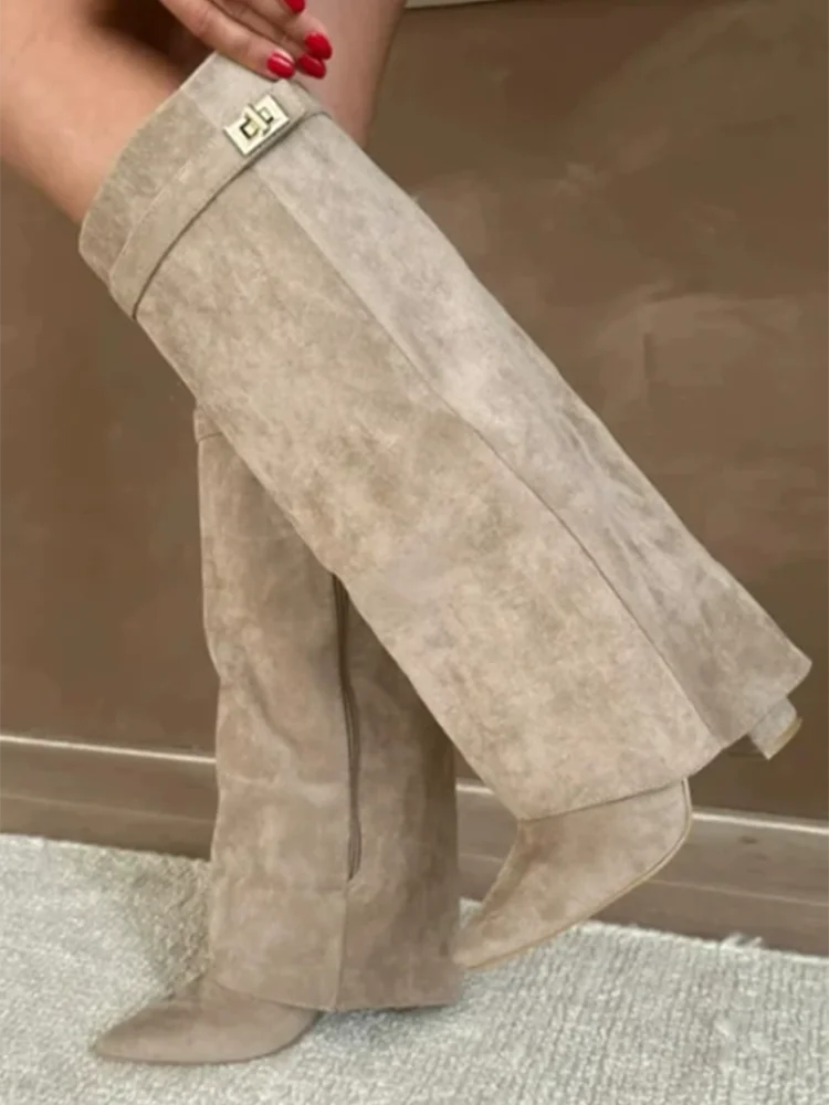 A close-up of beige knee-high boots with a chunky heel and a metal buckle worn on a leg.