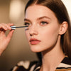 A woman applies waterproof volumizing mascara using a defining brush to her eye.