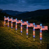 Una hilera de luces solares con la bandera estadounidense iluminando la exhibición en un campo de césped por la noche.