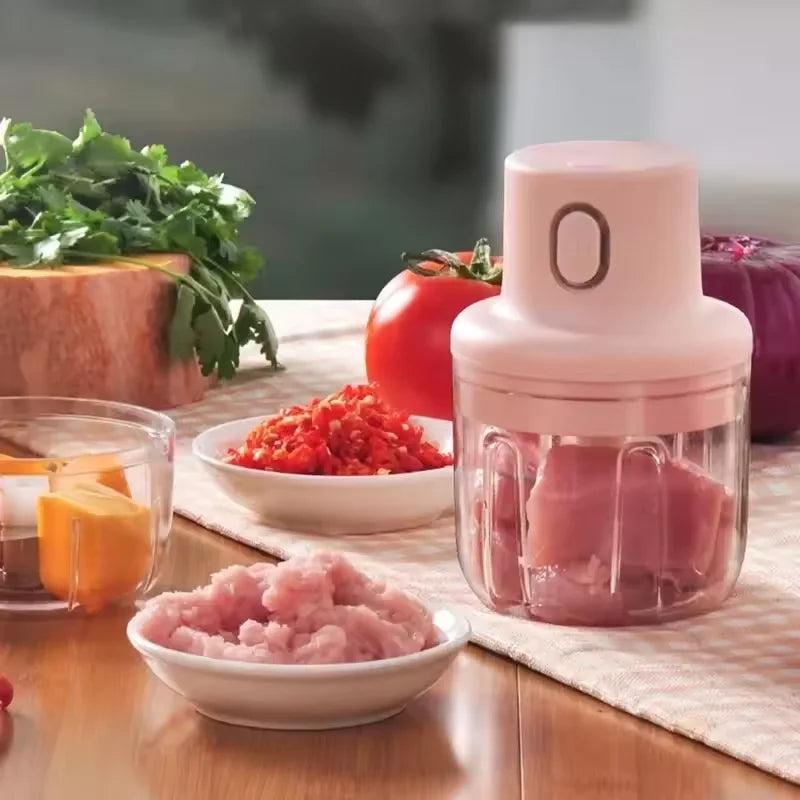 En rosa bærbar elektrisk foodprosessor med lokk, vist ved siden av tomater og rosa kjøtt.