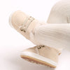 A close-up of beige soft cotton baby winter snow boots worn on a foot.