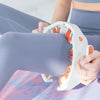 Una persona usa un rodillo de masaje muscular blanco en la pierna, vestida con ropa deportiva azul claro.