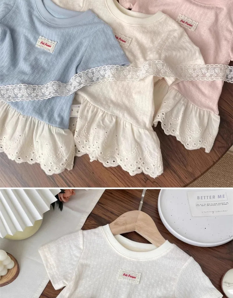 A stack of girls cotton lace hem short sleeve tees in light blue, cream, and pink.