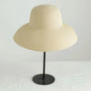 A beige wide brim straw sun hat displayed on a black stand.