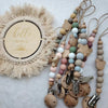 A necklace featuring wooden and silicone teether beads strung on twine, with a circular felt decoration nearby.