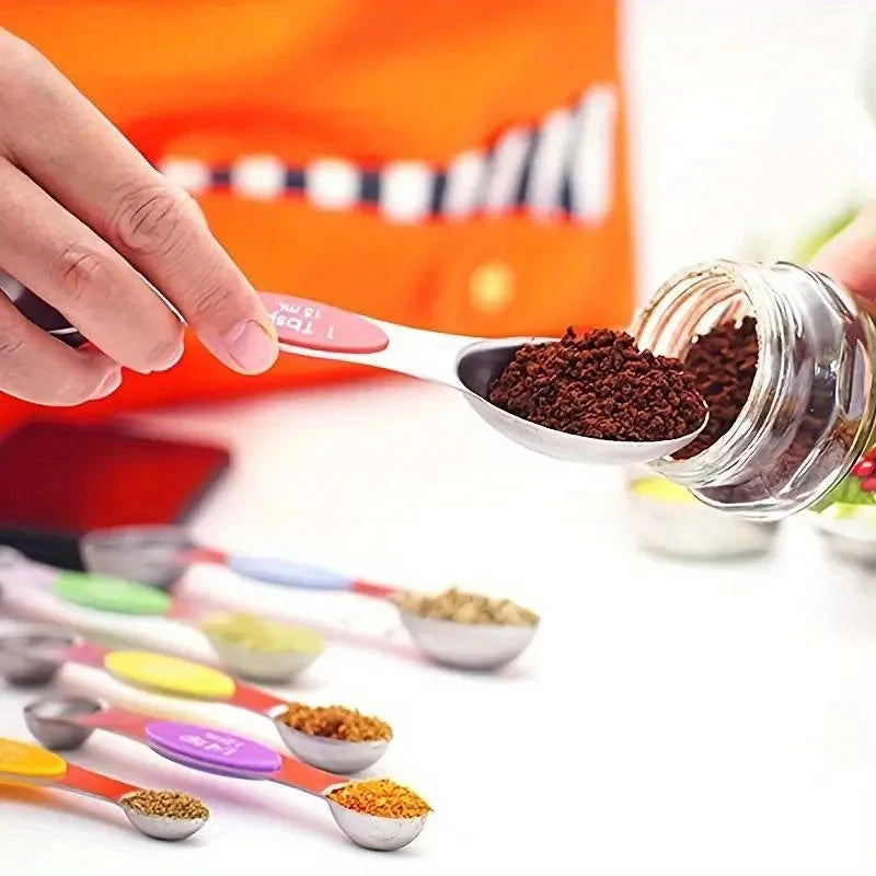A hand uses a stainless steel measuring spoon to scoop dark powder into a glass jar, with other spoons visible nearby.