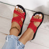 A close-up of a woman's feet wearing red breathable mesh flat sandals with white pedicure on a white wooden floor.
