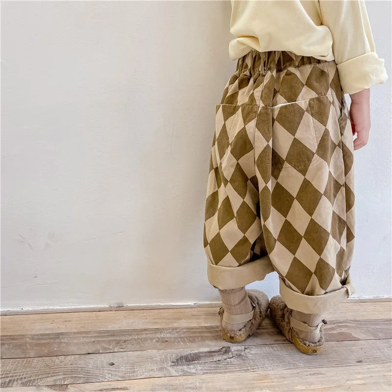 A child wearing beige top and olive green diamond patterned harem pants with light brown shoes.