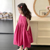 A young girl wearing a pink cotton sleeveless sundress standing in front of a large mirror.