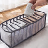 A hand is placing a folded gray cloth item into a clear plastic organizer designed for underwear and socks.