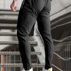 A man wearing black high-stretch joggers with zipper pockets and white sneakers, standing on a staircase.