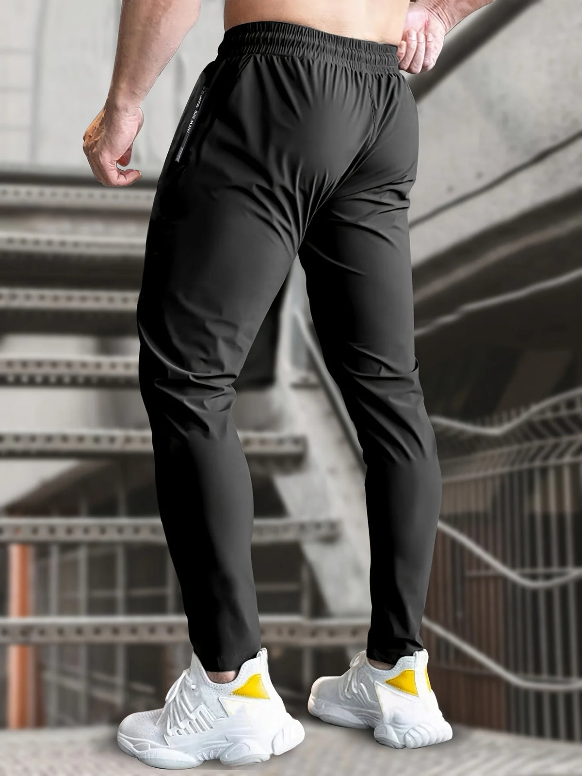 A man wearing black high-stretch joggers with zipper pockets and white sneakers, standing on a staircase.