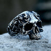 A detailed gothic carved skull ring made of 316L stainless steel resting on a gray surface.
