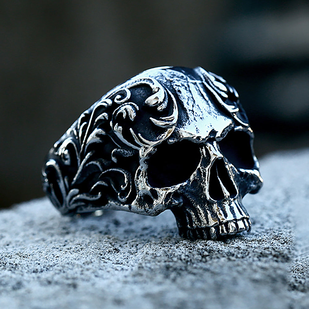 A detailed gothic carved skull ring made of 316L stainless steel resting on a gray surface.