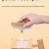 A hand is stirring a dark liquid in a glass mug using a rechargeable self-stirring device with a wooden handle.