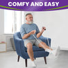 A man is using a white sock aid on his foot while sitting in an armchair.