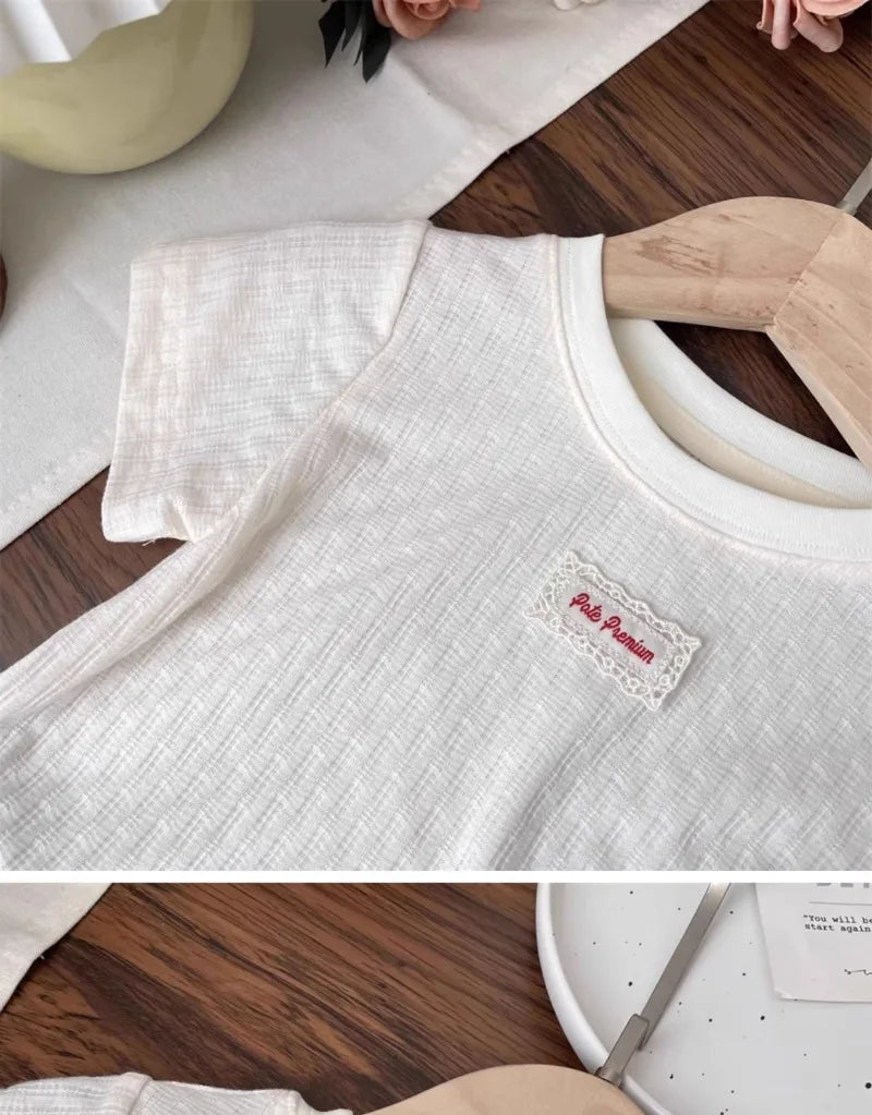A white girls cotton lace hem short sleeve t-shirt displayed on a wooden hanger.
