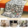 A black and white patterned blanket featuring various cartoon characters and objects, shown in use in a bedroom, game room, a
