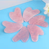 Pink jade gua sha massageværktøj arrangeret i en cirkel på en lyseblå overflade.