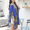 A woman models a blue and gold shimmer chiffon scarf and head wrap over a white top in a bright indoor setting.