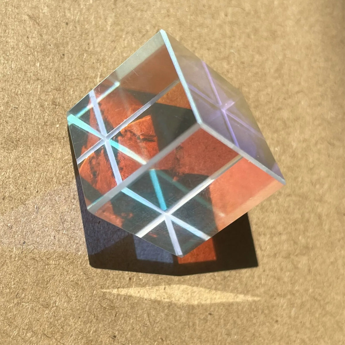 Transparent optiskt prismakub med rödbrunt och blått ljus som bryts mot en träyta.