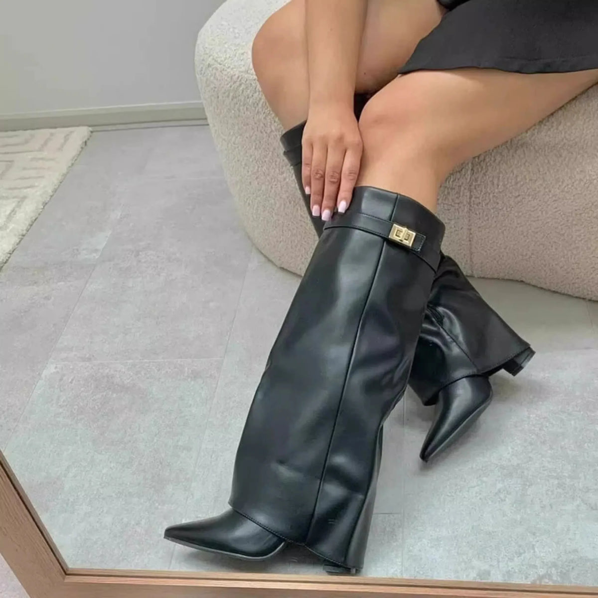 A close-up shot of a woman wearing black knee-high chunky heel boots with a gold metal buckle.