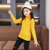 A young girl wearing a yellow knit turtleneck sweater and black jeans posing with her fingers raised.
