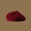 A deep red wool beret hat resting on a plain brown background.