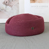 A deep magenta knitted pillbox sun hat with a wide brim resting on a gray surface.