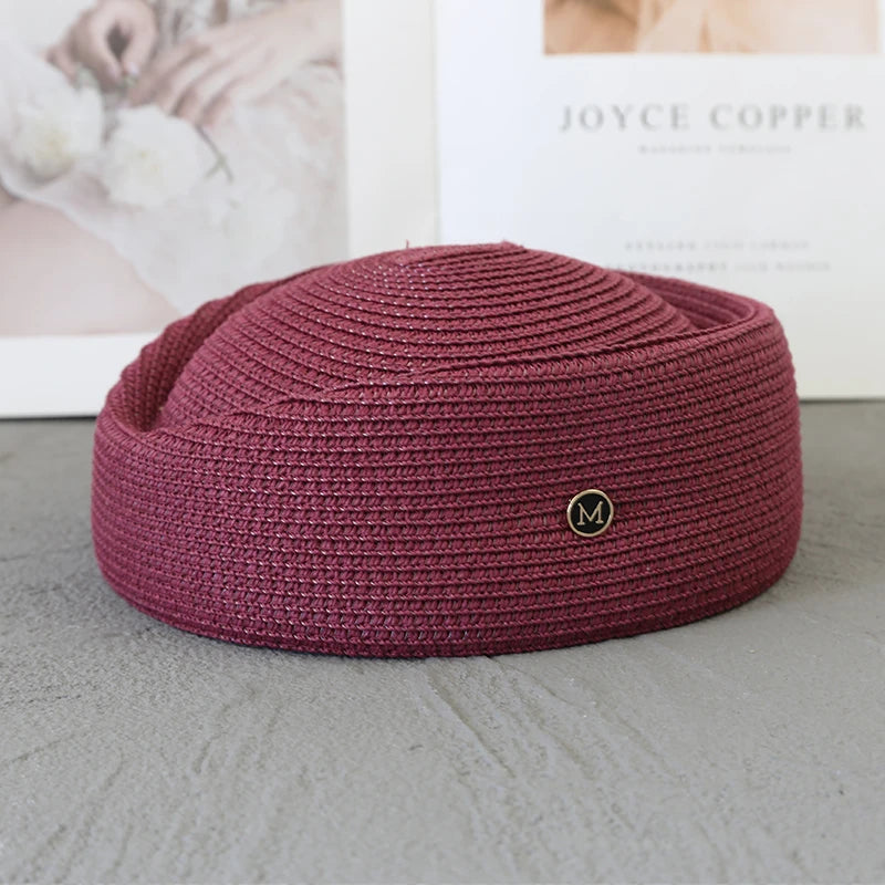 A deep magenta knitted pillbox sun hat with a wide brim resting on a gray surface.