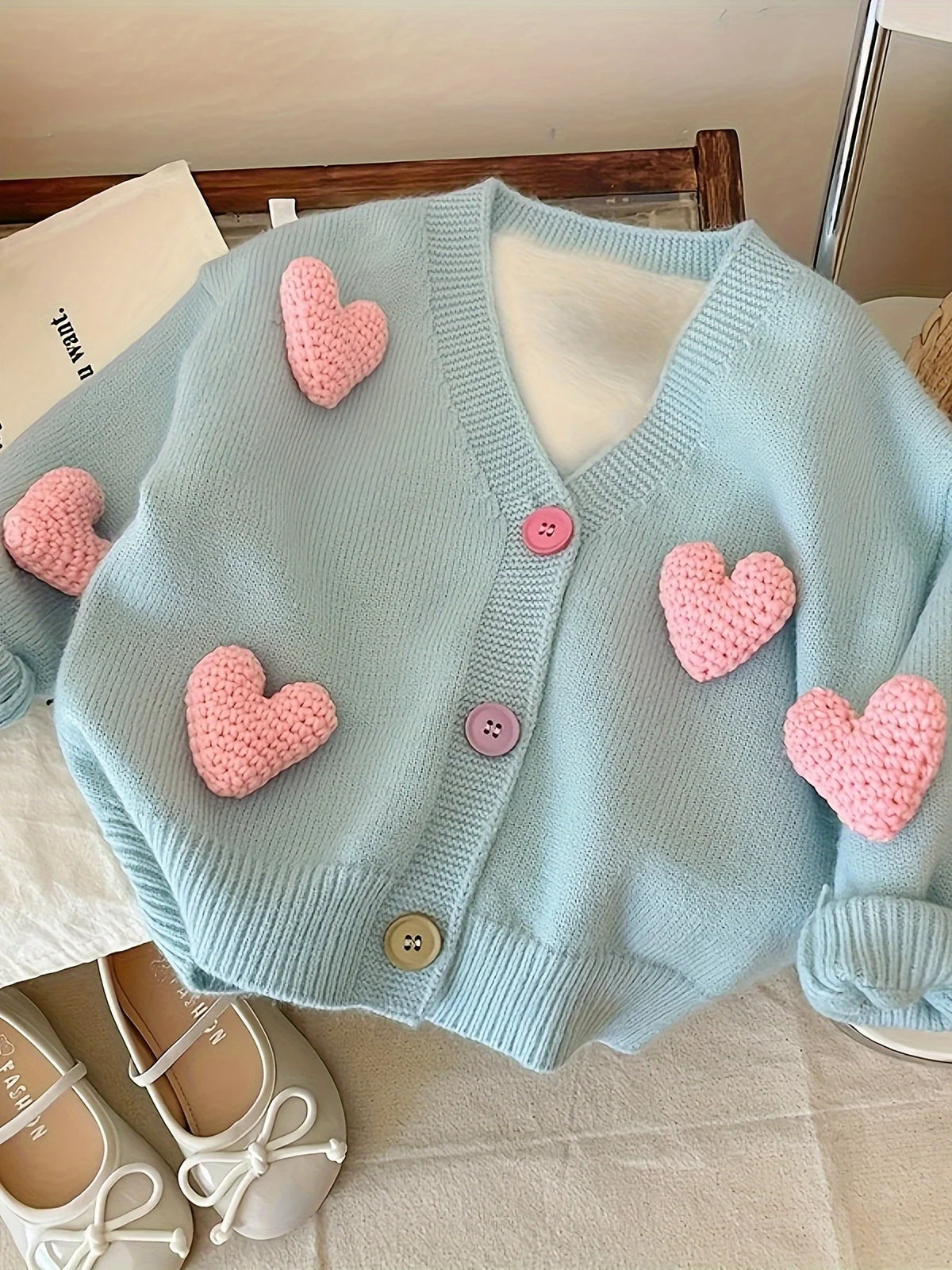 Light blue knit cardigan sweater with pink heart appliqués displayed on a light surface.