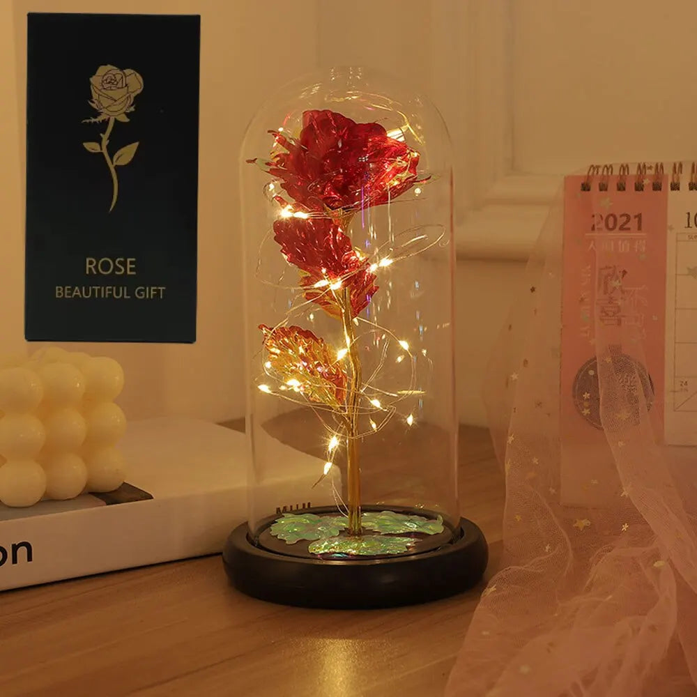 Glasskuppel med rød rose og LED-feélys på mørk base.