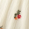Close-up of a cream linen dress fabric featuring small embroidered floral sprigs in shades of pink, orange, and green.