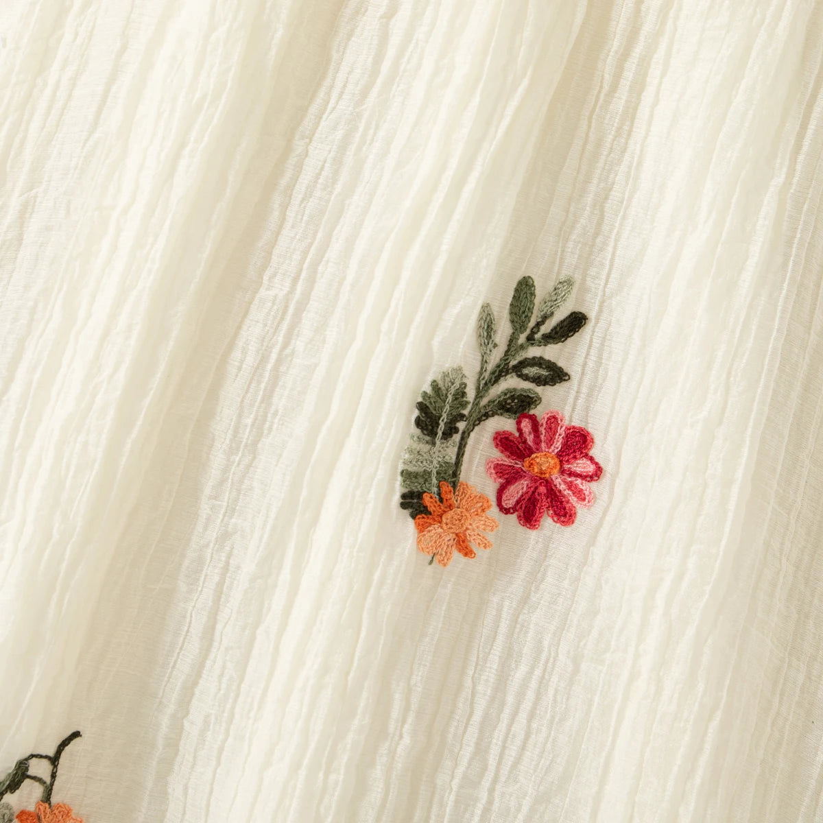 Close-up of a cream linen dress fabric featuring small embroidered floral sprigs in shades of pink, orange, and green.
