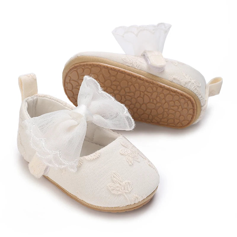 A pair of soft non-slip baby first walker shoes in cream color with lace detailing and a suede sole.