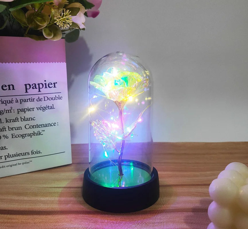 En glasskuppel med en fortryllet galakserose og glødende LED-feelys på en mørk base.