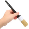 A hand is holding a black and white detailing brush with a yellow bristle for cleaning.