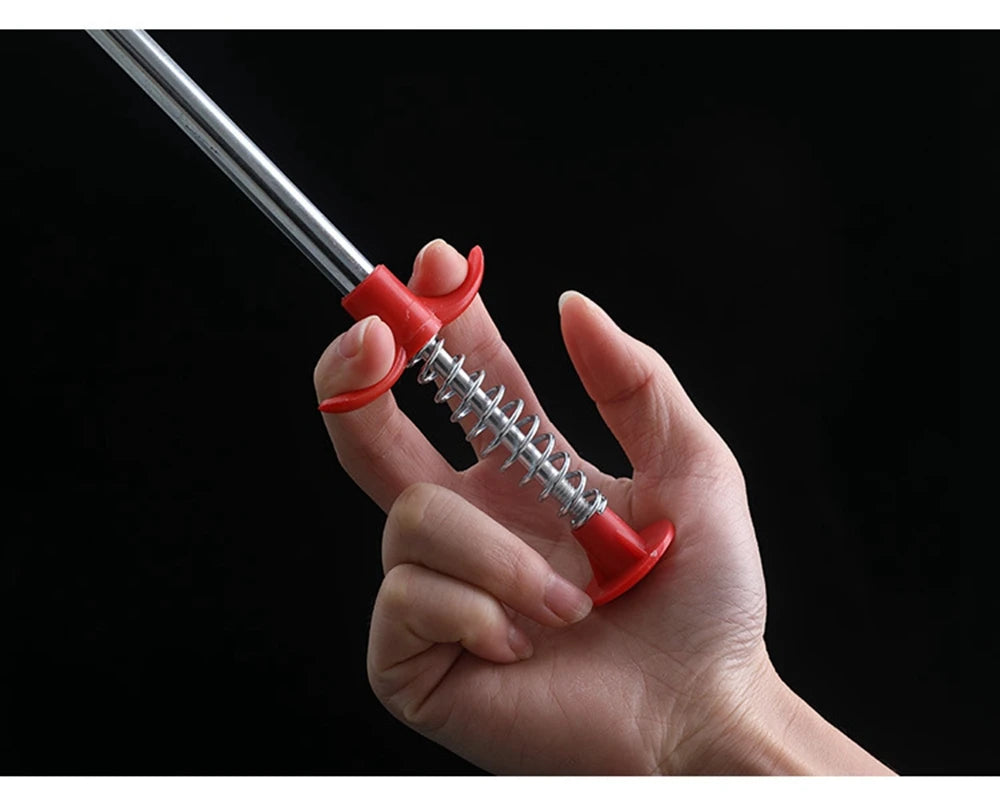 A hand is holding a flexible drain snake with a red handle and silver wire, against a black background.