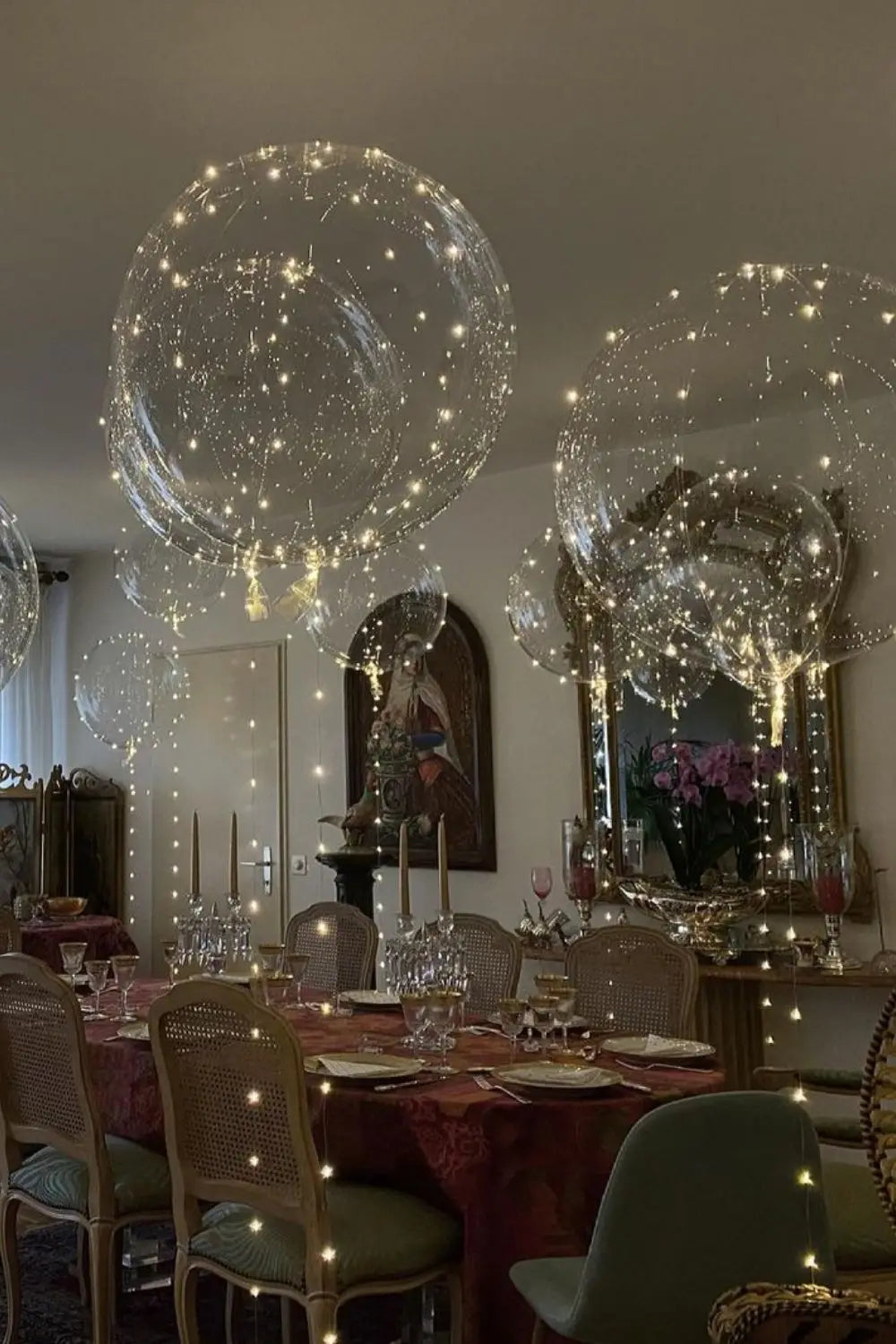 A ceiling display of clear balloons filled with twinkling LED lights in an elegant room setting.
