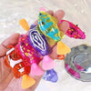 A hand holds a collection of colorful photosensitive robotic clownfish toys in various shades of yellow, pink, purple, and gr