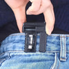 En hånd holder en justerbar spændeklips til bæltestropper til bukser og nederdele, det sorte plastprodukt vises mod denim.